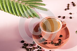 Coral colored cup with effuse coffee`s beans with shadows on pastel rose background. Flat lay. Top view. Coffee concept. Pop art