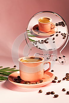 Coral colored cup with effuse coffee`s beans with shadows reflected in the mirror on pastel rose background. Coffee concept.