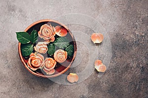 Coral heads of roses in a brown ceramic bowl on a dark rustic background, vintage style. Top view, flat lay, copy space