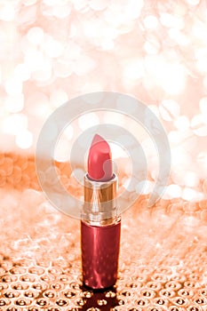 Coral lipstick on rose gold Christmas, New Years and Valentines Day holiday glitter background, make-up and cosmetics product for