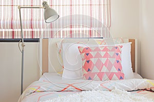 Coral pink triangle pattern pillow setting on bed with foldable lamp