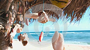 Coral and  shells handmade beads hanging from a roof made of palm leaves sway in the wind. ocean view from savage hut on the beach