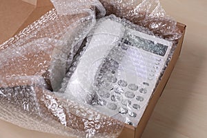 Corded phone with bubble wrap in cardboard box on wooden table, closeup