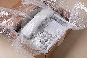 Corded phone with bubble wrap in cardboard box on wooden table, closeup