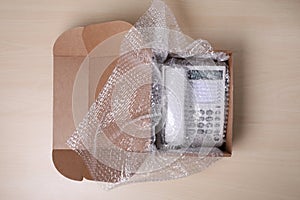 Corded phone with bubble wrap in cardboard box on wooden table, top view