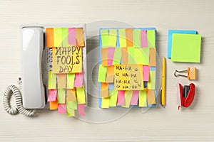 Corded phone and notebook covered with sticky notes on wooden table, flat lay. April fool`s day celebration