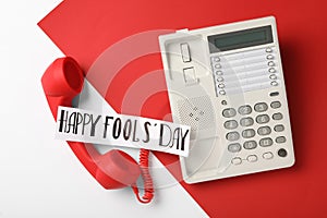 Corded phone with red handset and words Happy Fool`s Day on color background, flat lay