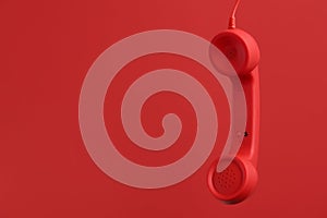 Corded telephone handset hanging on red background, space for text. Hotline concept