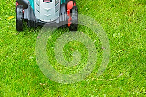 Cordless battery power lawn mower close up on green grass background
