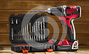 Cordless drill driver in red with rubberized handle in profile with drill bits set