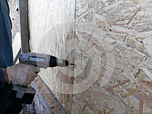 Cordless screwdriver or drill in the hands of a male worker, twists the screws into a wooden panel, board