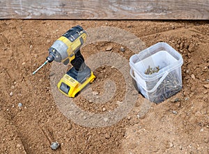 Cordless screwdriver and wood screws in the dirt at construction site