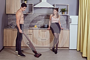 Cordless upright vacuum cleaner is used by married couple to clean kitchen.