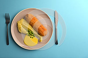 Cordon bleu cutlet, deep fried meat served with mashed potatoes and green peas on gray plate over blue background.