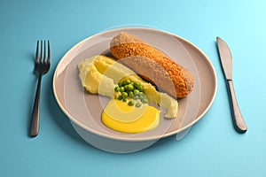 Cordon bleu cutlet, deep fried meat served with mashed potatoes and green peas on gray plate over blue background.