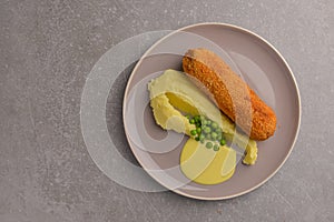 Cordon bleu cutlet, deep fried meat served with mashed potatoes and green peas on gray plate over gray background.