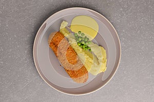 Cordon bleu cutlet, deep fried meat served with mashed potatoes and green peas on gray plate over gray background.