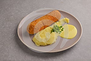 Cordon bleu cutlet, deep fried meat served with mashed potatoes and green peas on gray plate over gray background