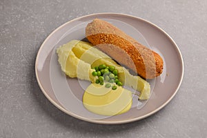 Cordon bleu cutlet, deep fried meat served with mashed potatoes and green peas on gray plate over gray background