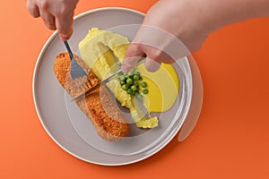 Cordon bleu cutlet, deep fried meat served with mashed potatoes and green peas on gray plate over orange background.