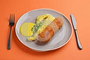 Cordon bleu cutlet, deep fried meat served with mashed potatoes and green peas on gray plate over orange background.