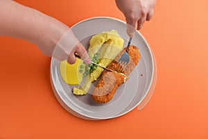 Cordon bleu cutlet, deep fried meat served with mashed potatoes and green peas on gray plate over orange background.