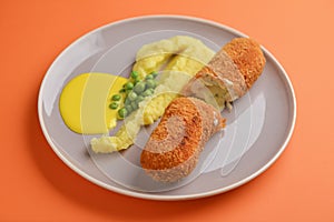 Cordon bleu cutlet, deep fried meat served with mashed potatoes and green peas on gray plate over orange background.