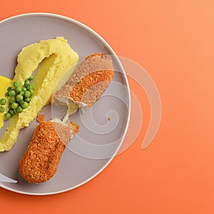 Cordon bleu cutlet, deep fried meat served with mashed potatoes and green peas on gray plate over orange background.