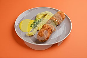 Cordon bleu cutlet, deep fried meat served with mashed potatoes and green peas on gray plate over orange background.