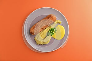 Cordon bleu cutlet, deep fried meat served with mashed potatoes and green peas on gray plate over orange background