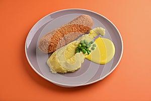 Cordon bleu cutlet, deep fried meat served with mashed potatoes and green peas on gray plate over orange background