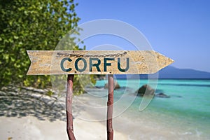 Corfu wooden arrow road sign against beach with white sand and turquoise water background. Travel to Greece concept