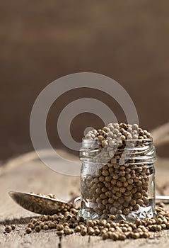 Coriander seeds in jar, dry oriental spice, rustic style, old kitchen table, selective focus