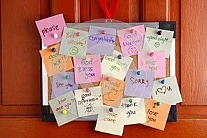 Cork board with messages on colorful papers and push pins hanging by a door