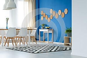 Cork honeycombs on blue wall of trendsetting dining room interior with patterned carpet, plants and white furniture