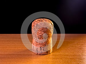 Cork plug from champagne or sparkling wine stands on a wooden surface with black background and a hint of lighting from the upper