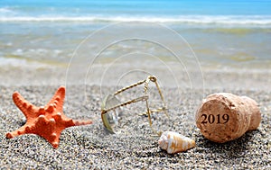 Cork stopper of champagne with number 2019 and seashell with starfish on sand beach.