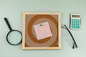 Corkboard with a note near a magnifying glass and eyeglasses