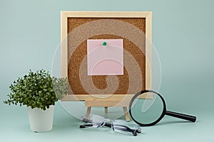 Corkboard with a note near a magnifying glass and eyeglasses