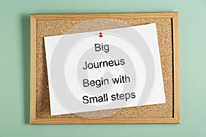 Corkboard and phrase Big Journeys Begin With Small Steps on light green background, top view. Motivational quote