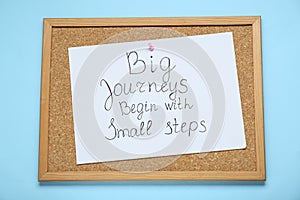 Corkboard with pinned message Big Journeys Begin With Small Steps on light blue background, top view. Motivational quote