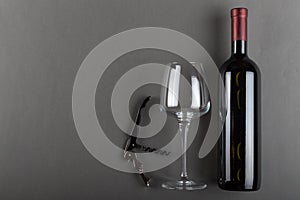 Corked red wine bottle, corkscrew and empty wine glass on gray background. Alcoholic drink. Winemaking concept