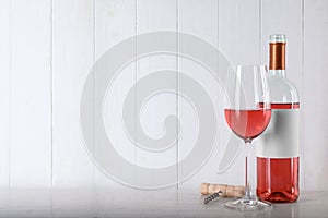 Corkscrew near bottle and glass of delicious rose wine on table against white wooden background. Space for text