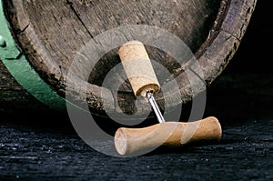 Corkscrew next to a wooden wine barrel. Wine on a wooden barrel. Burnt, black wooden background. Vintage. Copyspace for a text. Gr