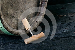 Corkscrew next to a wooden wine barrel. Wine on a wooden barrel. Burnt, black wooden background. Vintage. Copyspace for a text. Gr