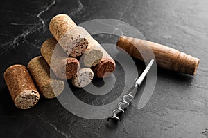 Corkscrew and stack of wine bottle stoppers on slate table, closeup