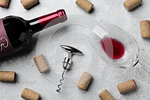 Corkscrew with wine bottle, glass and stoppers on light grey stone table, flat lay