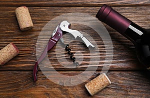 Corkscrew, wine bottle and stoppers on wooden table, flat lay