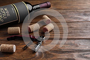 Corkscrew, wine bottle and stoppers on wooden table. Space for text