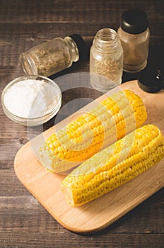 Corn. Appetizing boiled corn with salt and seasonings on a wooden table. Top view